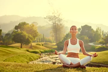  Yoga at park with view of the mountains, with sunlight. Young woman in lotus pose sitting on green grass. Concept of calm and meditation. © luengo_ua