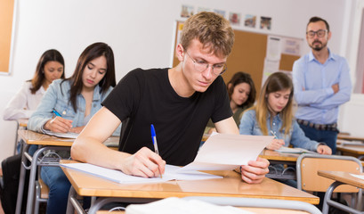 Young boy is writing test and thinking about questions at the desk