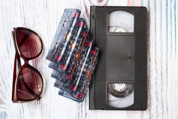 Old audio tapes folded into a stack of video tapes near near sunglasses. Retro multimedia technology.