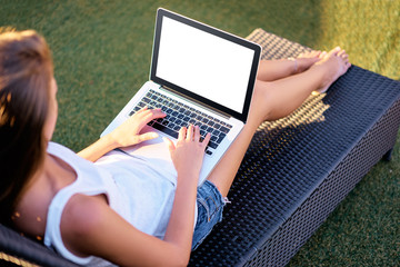 Work and relaxation. Young woman using laptop sitting at sunlounger outdoors. Copy space on the screen.