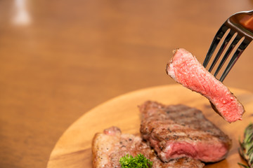 Cooked beef steak with rosemary, parsley and cherry tomato on fork, Wood background, Copy space on the left