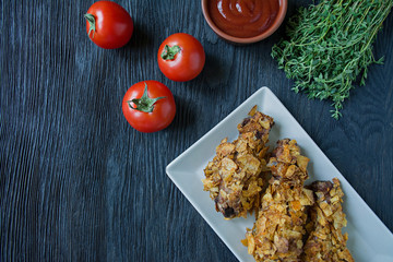Roasted chicken drumsticks on a plate. Breaded chicken drumsticks, fried chicken. Dark wooden background.