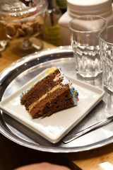 piece of cake in a silver tray with two glasses in a background of a coffee shop