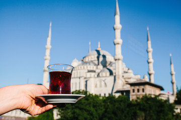 Naklejka premium Woman holding cup of traditional Turkish tea on terrace with view of the Blue Mosque in Istanbul in Turkey.