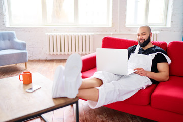 Working at home. Young man using laptop computer while sitting on sofa.