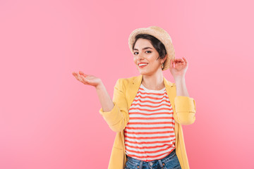 attractive mixed race girl in straw hat posing at camera isolated on pink