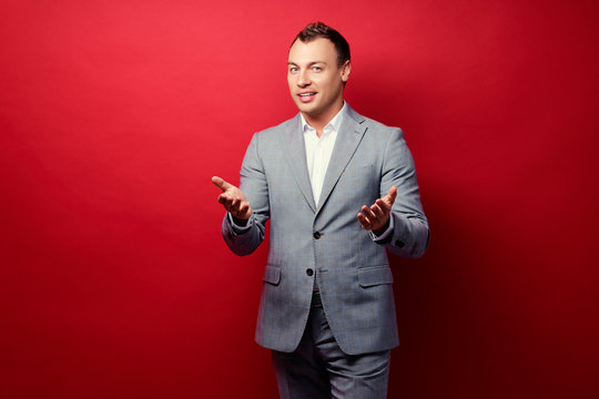 Presenting your product. Half length of happy young man in formal wear pointing copy space or gesturing welcome sign while standing against red wall.
