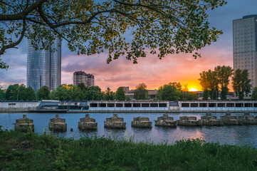 Fototapeta na wymiar Dramatic sunset over city Riga. Colorful storm clouds surrounding skyscrapers. Green park next to river and urban scene. Breathtaking view on downtown. 