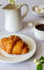 A croissant and coffee on a marble background. The flowers. Breakfast.