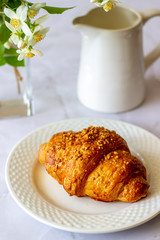 A croissant and coffee on a marble background. The flowers. Breakfast.