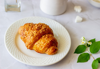 A croissant and coffee on a marble background. The flowers. Breakfast.