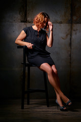 Fototapeta premium Studio Portrait of Beautiful young woman with ginger hair in little black dress against dark background.