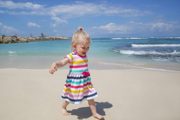 Happy playful toddler girl running on the white sandy beach 