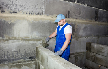 Industrial worker using trowel and tools for building exterior walls with blocks and mortar