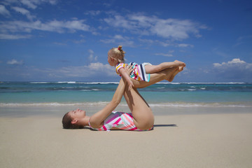 Mother doing yoga exercise together with her baby girl, outdoor family activity, family summer vacation concept
