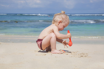 Little toddler girl playing with sand at the beach 