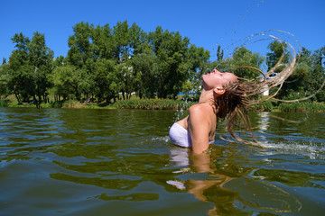 Young woman raises her hair from the water on the lake