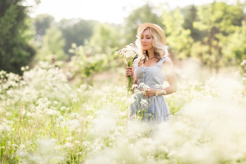 Obraz premium Female portrait outdoors. a woman in a straw hat in a flower field with a bouquet of wild flowers. Summer in the country