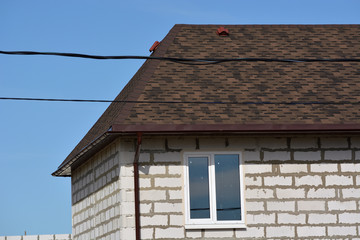 A fragment of a foam block house with a brown tile and a window with electric cables against a blue sky. Construction and building materials