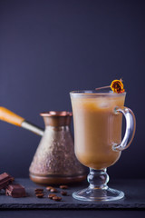 Copper coffee pot (Cezve) and coffee beans. Coffee with milk on dark background. Latte and black chocolate on slate board. Milk drink in glass beaker and dried rose