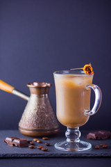 Copper coffee pot (Cezve) and coffee beans. Coffee with milk on dark background. Latte and black chocolate on slate board. Milk drink in glass beaker and dried rose