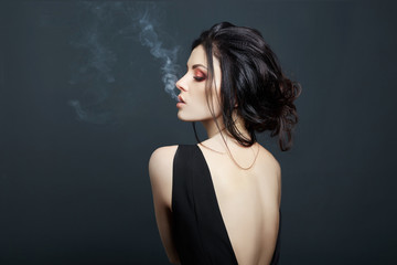 Brunette woman Smoking on dark background in black dress. Erotic girl