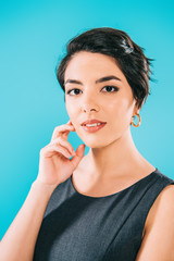 portrait of beautiful mixed race woman looking at camera while holding hand near face isolated on blue