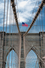 Obraz premium Brooklyn Bridge, New York City. American Flag, Cloudy Blue Sky, Vertical Banner