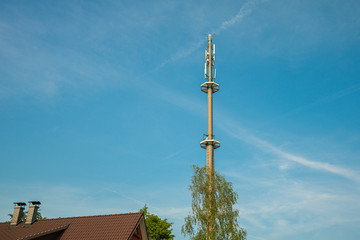 a radio mast for the mobile phone network towers above a residential building into the blue sky in...