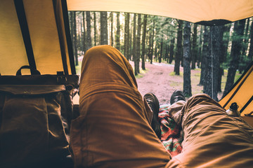 Alternative point of view for people relaxing inside a tent with amazing view outside - forest with trees and wood on background - altrnative vacation travel man with backpack enjoying the nature