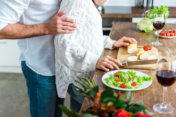 cropped view of man embracing woman near table with salad and bread