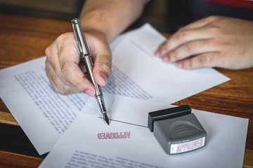 Close up hands of businessman signing and stamp on paper document to approve business investment...