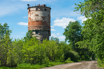 Old red brick tower. Russian road and green trees