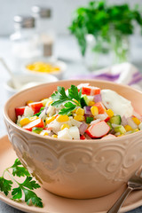 Salad with crab sticks, sweet corn, cucumbers, boiled eggs, onion and rice in bowl on concrete background. Russian cuisine. Selective focus.