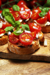 Traditional italian antipasto bruschetta appetizer with cherry tomatoes, cream cheese, basil leaves and balsamic vinegar on cutting board. Antipasti