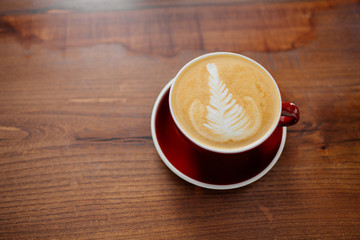 Cappucino in red cup on a table.