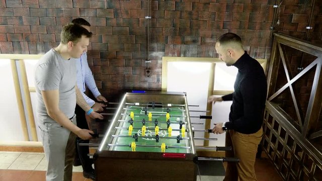 Sport, game concept. Foosball. Three men playing a table football or kicker with miniature players. 4K