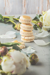 macarons and white peony flowers on wooden surface   