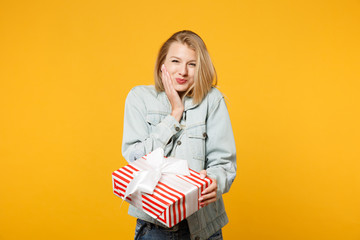 Joyful pretty young girl in denim casual clothes hold red striped present box with gift ribbon...