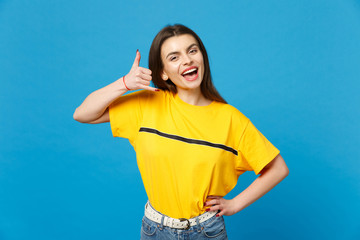 Portrait of cheerful young woman in vivid casual clothes looking camera, doing phone gesture like says call me back isolated on bright blue background. People lifestyle concept. Mock up copy space.