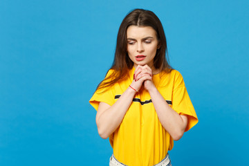 Portrait of worried young woman in vivid casual clothes looking down, holding hands crossed,...