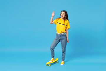 Laughing young woman looking aside, waving and greeting with hand as notices someone, standing with...