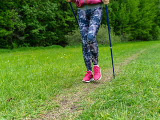 Nordic walking. Nordic walking trekking  hiking concept - close up of woman athletic legs. Fitness woman training on forest trail. Woman fitness jogging workout wellness. Female walker on green grass.