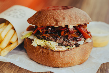 Delicious fresh homemade cheese burger with meat, cheese, tomatoes, lettuce and onion rings in Kraft paper and french fries . street food on wooden table  on wooden background