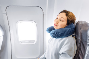 Asian girl sleeping in her seat on the plane near the window in a mask and with a pillow to sleep. The concept of travel with comfort and jetlag