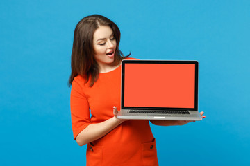 Young woman wearing red orange dress hold in hands using laptop pc computer with blank empty screen isolated on blue background, studio portrait. People lifestyle fashion concept. Mock up copy space.