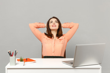 Young smiling woman in pastel clothes looking up, sleep with hands behind head, work at desk with laptop isolated on gray background. Achievement business career lifestyle concept. Mock up copy space.