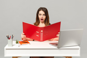 Young shocked woman in pastel clothes holding red folder for papers document work at desk with pc laptop isolated on gray background. Achievement business career lifestyle concept. Mock up copy space.