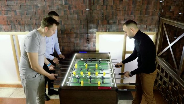 Sport, game concept. Foosball. Three men playing a table football or kicker with miniature players. 4K