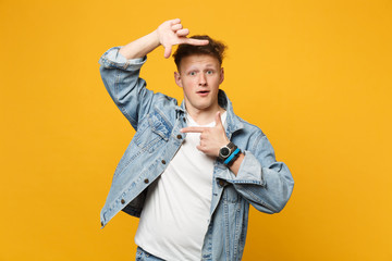 Amazed young man in denim casual clothes looking camera making hands photo frame gesture isolated on yellow orange background in studio. People sincere emotions, lifestyle concept. Mock up copy space.